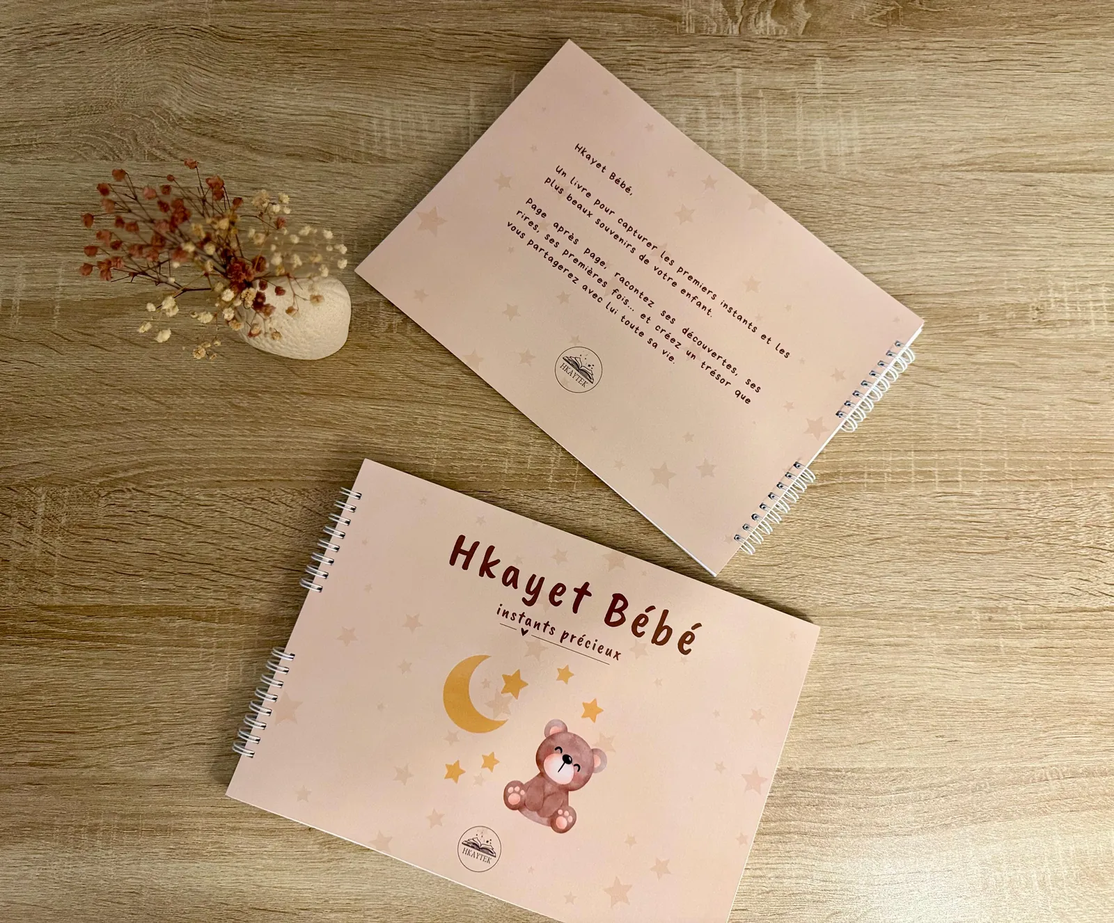 Le livre Hkayet Bébé, recto et verso, posé sur une table en bois avec des fleurs séchées