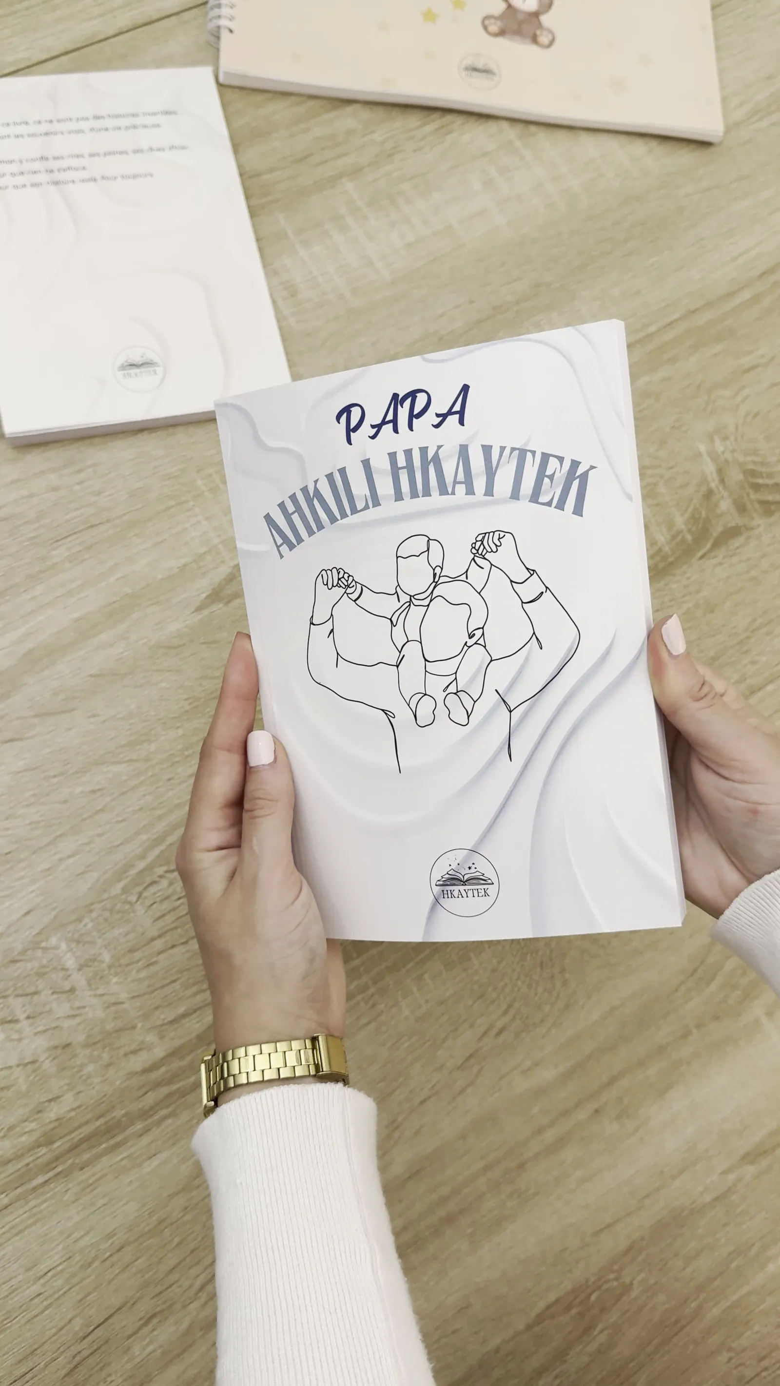 Le livre Papa, Ahkili Hkaytek tenu à deux mains au-dessus d'une table en bois
