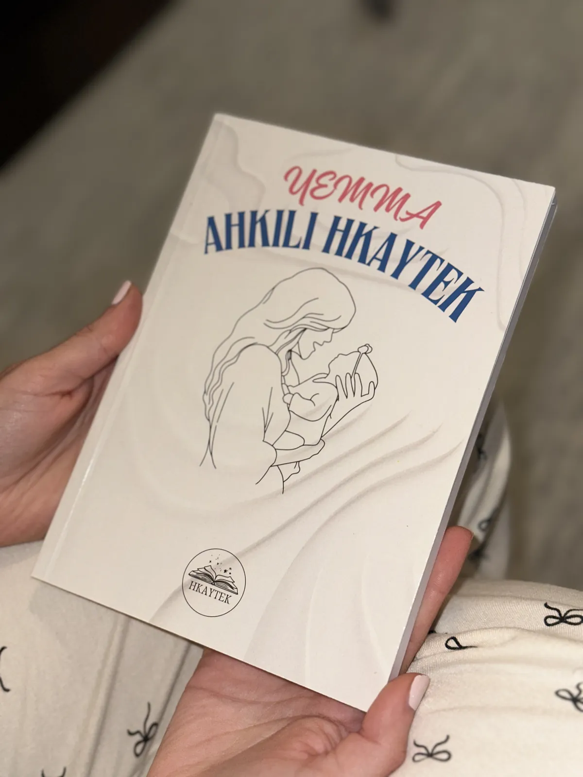 Le livre Yemma, Ahkili Hkaytek tenu dans une main